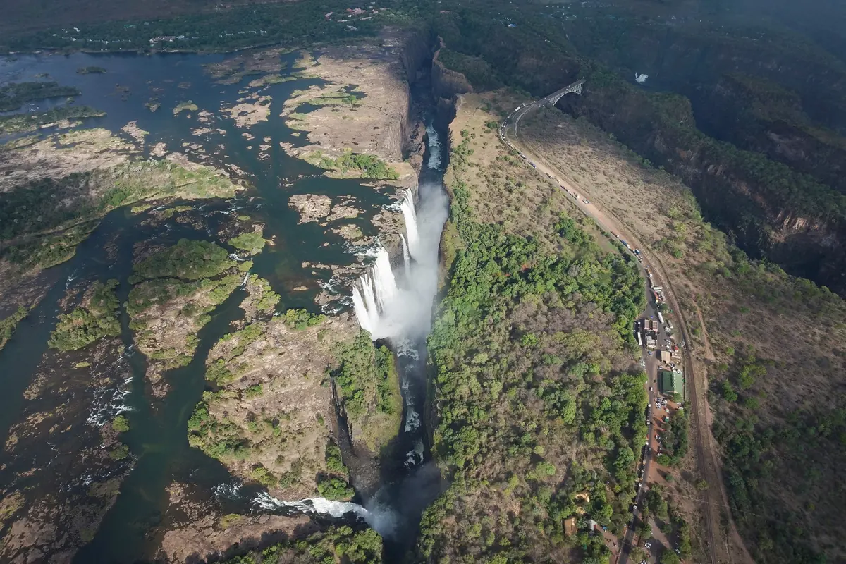 Una vista aerea delle Cascate Vittoria che precipitano in una gola stretta, con il ponte che si inarca in alto a destra (una veduta diurna delle cascate, non del teatro)