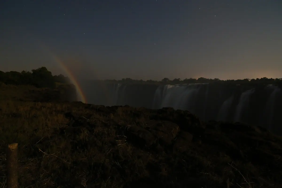Un tenue arcobaleno lunare che si alza accanto alle cascate di notte sotto un cielo stellato (le cascate dopo il tramonto, non il teatro)